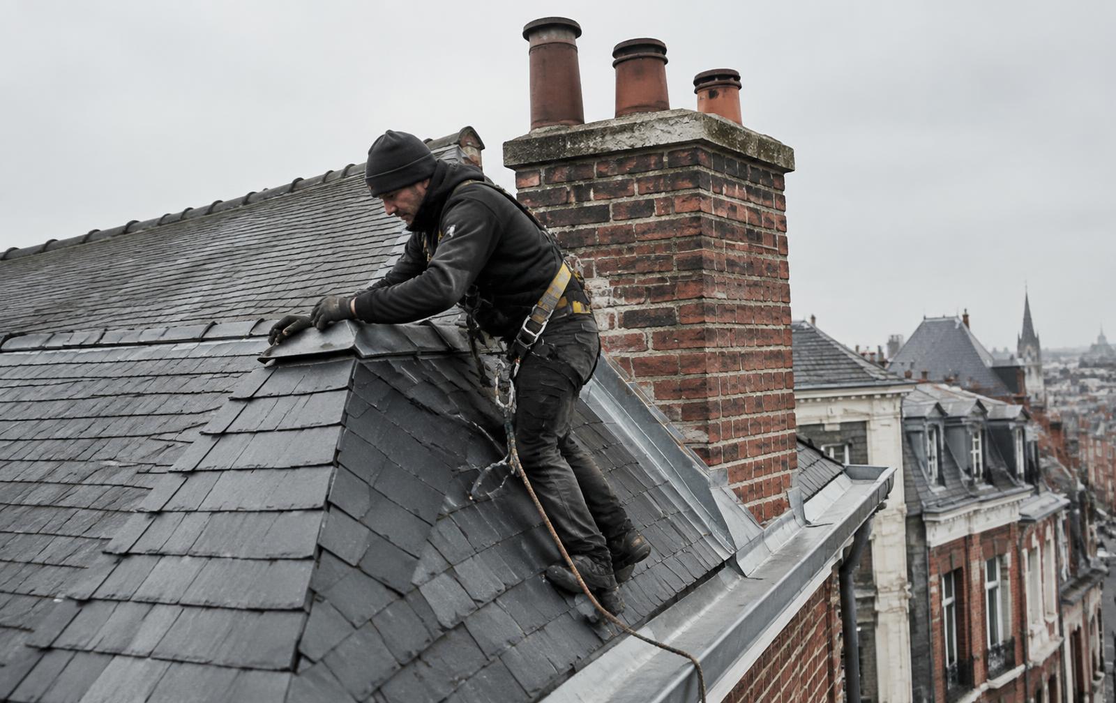 Couvreur réparant une toiture en ardoise près d'une cheminée à Ixelles